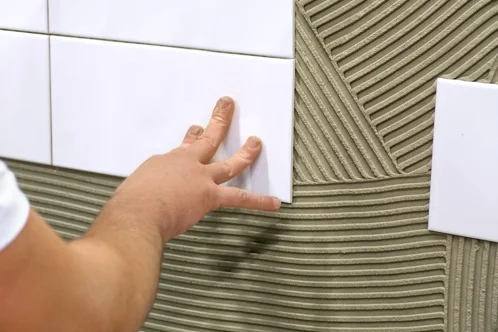 Person verlegt weiße Wandfliese